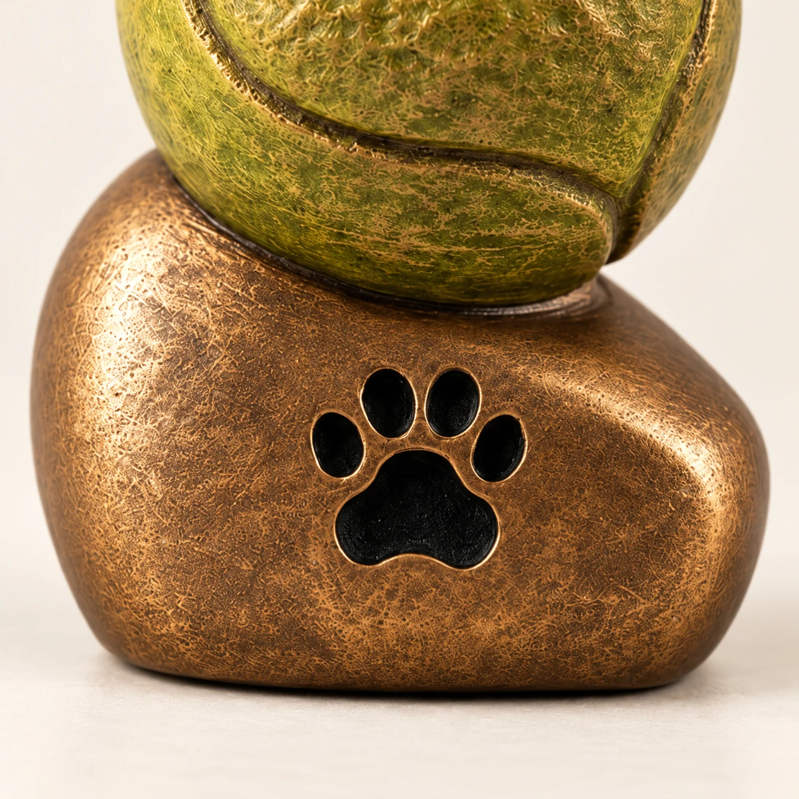 Zampetta™ dierenurn: bronskleurige voet met pootafdruk en tennisbal van dichtbij